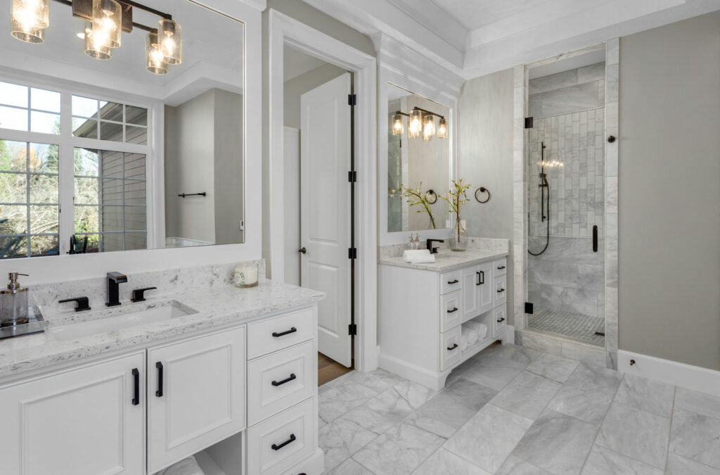 Modern bathroom with white Jack & Jill vanities, gold accents, and grey plank floors